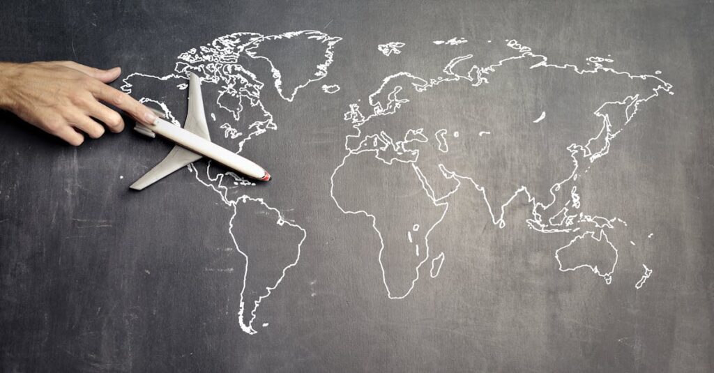 From above of crop anonymous person driving toy airplane on empty world map drawn on blackboard representing travel concept